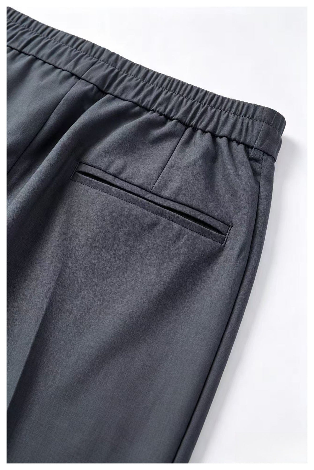 Close-up of charcoal-gray trousers showing the gathered elastic back waistband and a single welt pocket.
