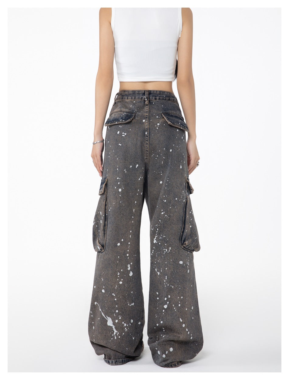 Back view of a model wearing loose charcoal-gray splatter-print cargo jeans with flap pockets at the rear and sides.