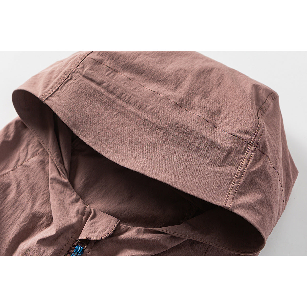 Close-up of the dusty rose jacket's hood, showing stitched panels and a glimpse of the blue zipper pull.