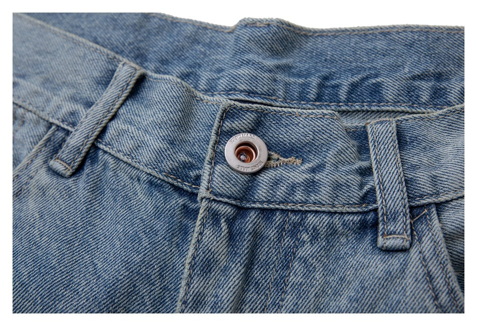 Close-up of the waistband button and belt loops on light blue washed jeans.