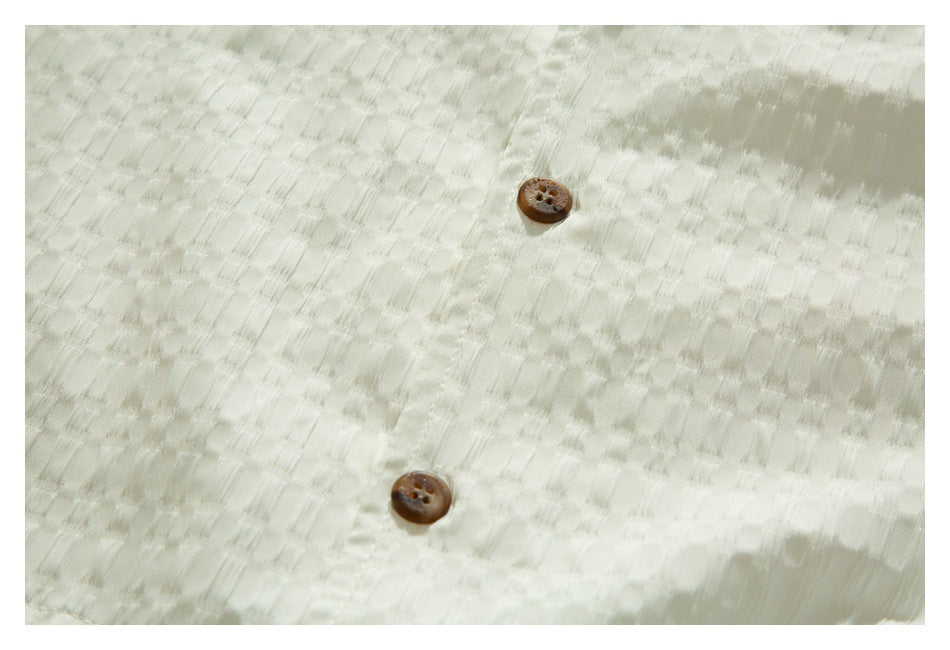 Close-up of two brown buttons on the textured ivory shirt front.