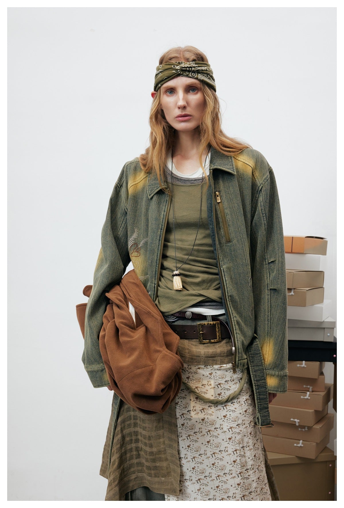 Front view of a model wearing a distressed olive jacket with floral embroidery, front zipper, and buckle belt hem.