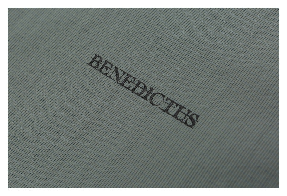 Close-up of a black BENEDICTUS logo on muted gray-green fabric with fine vertical ribbing.