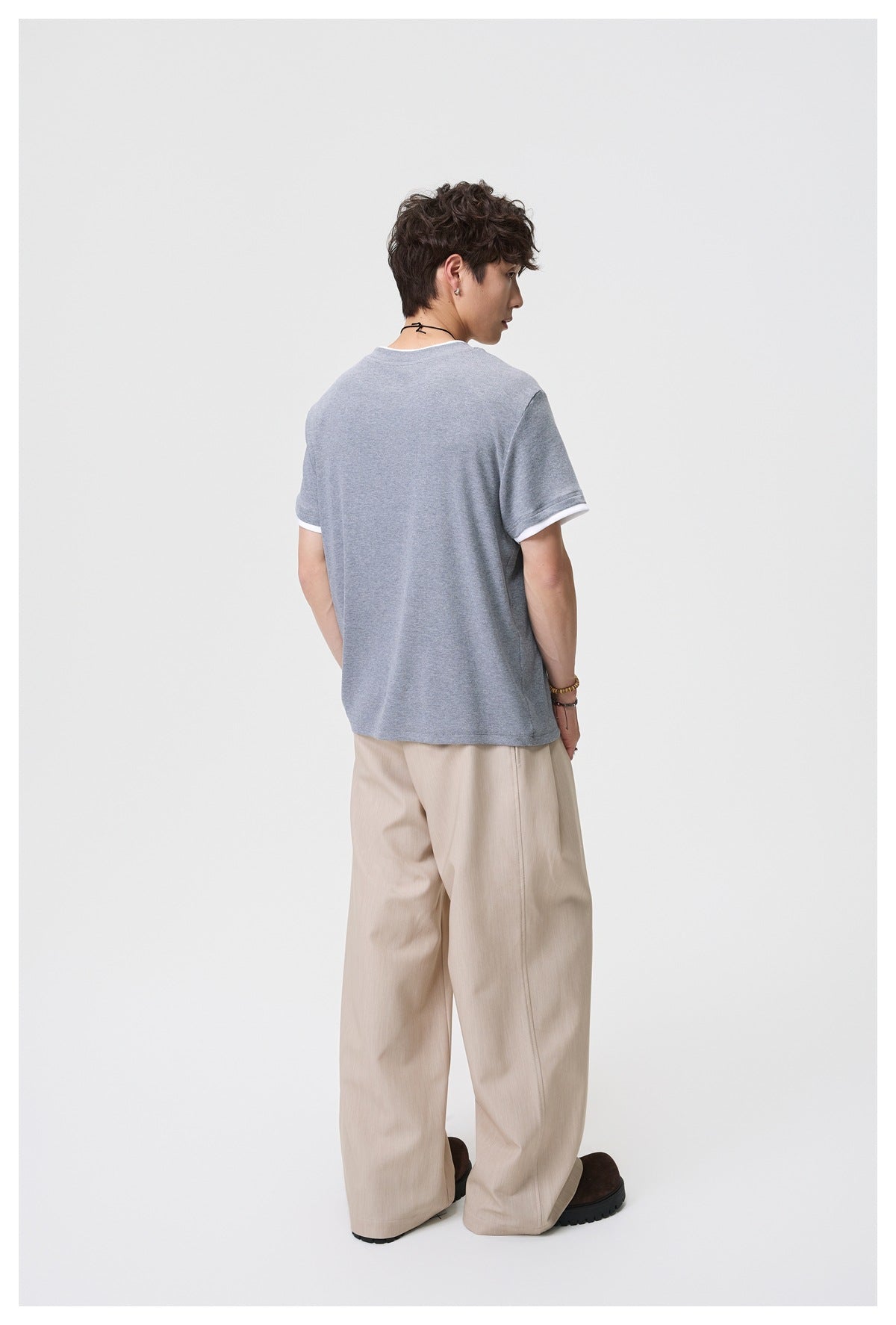 Back view of a model wearing a heather gray T-shirt with white sleeve trim and beige trousers.