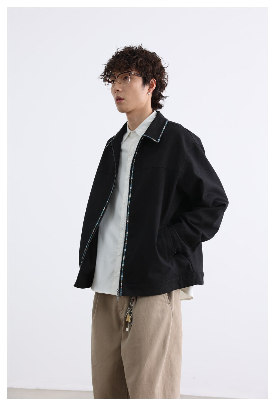 Angled view of a model wearing a loose black jacket with multicolor trim over a white shirt.