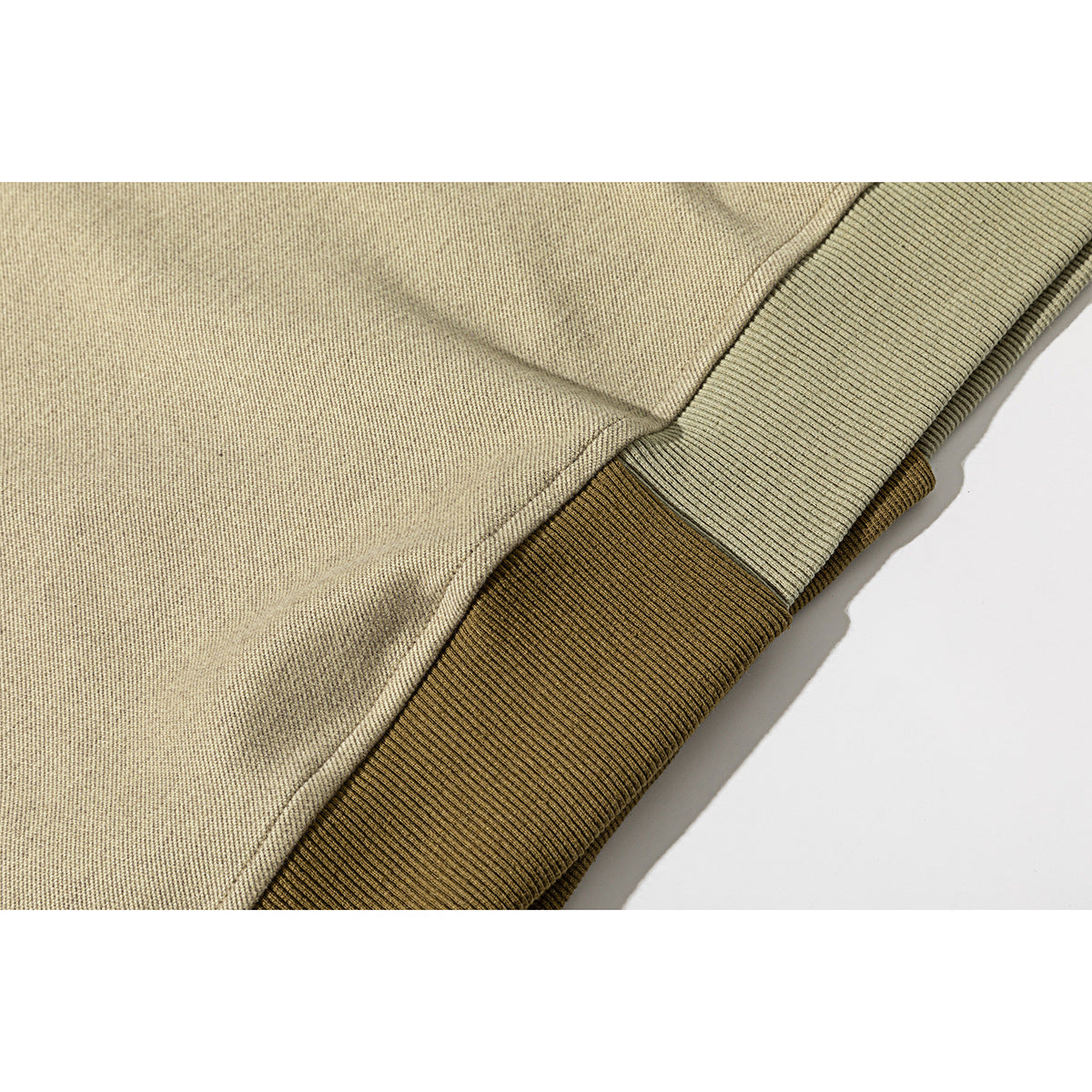 Close-up of a beige sweatshirt hem with layered sage and olive ribbed bands.
