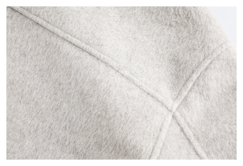 Close-up of intersecting seams on the pale beige coat's fuzzy fabric.