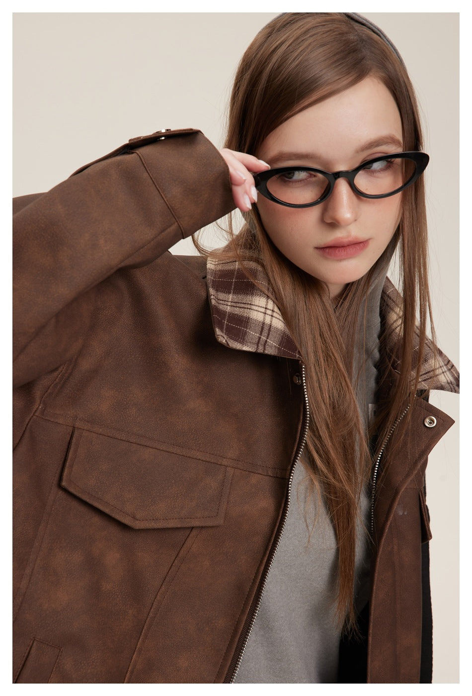 Close-up of the brown jacket's flap pocket, plaid collar and zip front as the model adjusts her glasses.