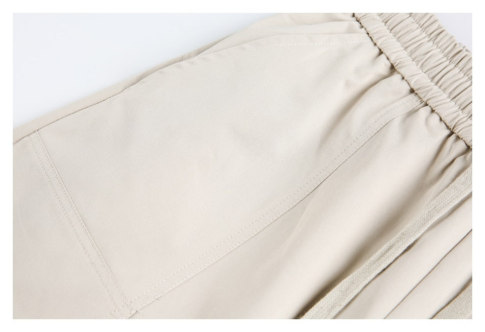 Close-up of light beige pants showing waistband stitching, a drawstring, and a curved seam.