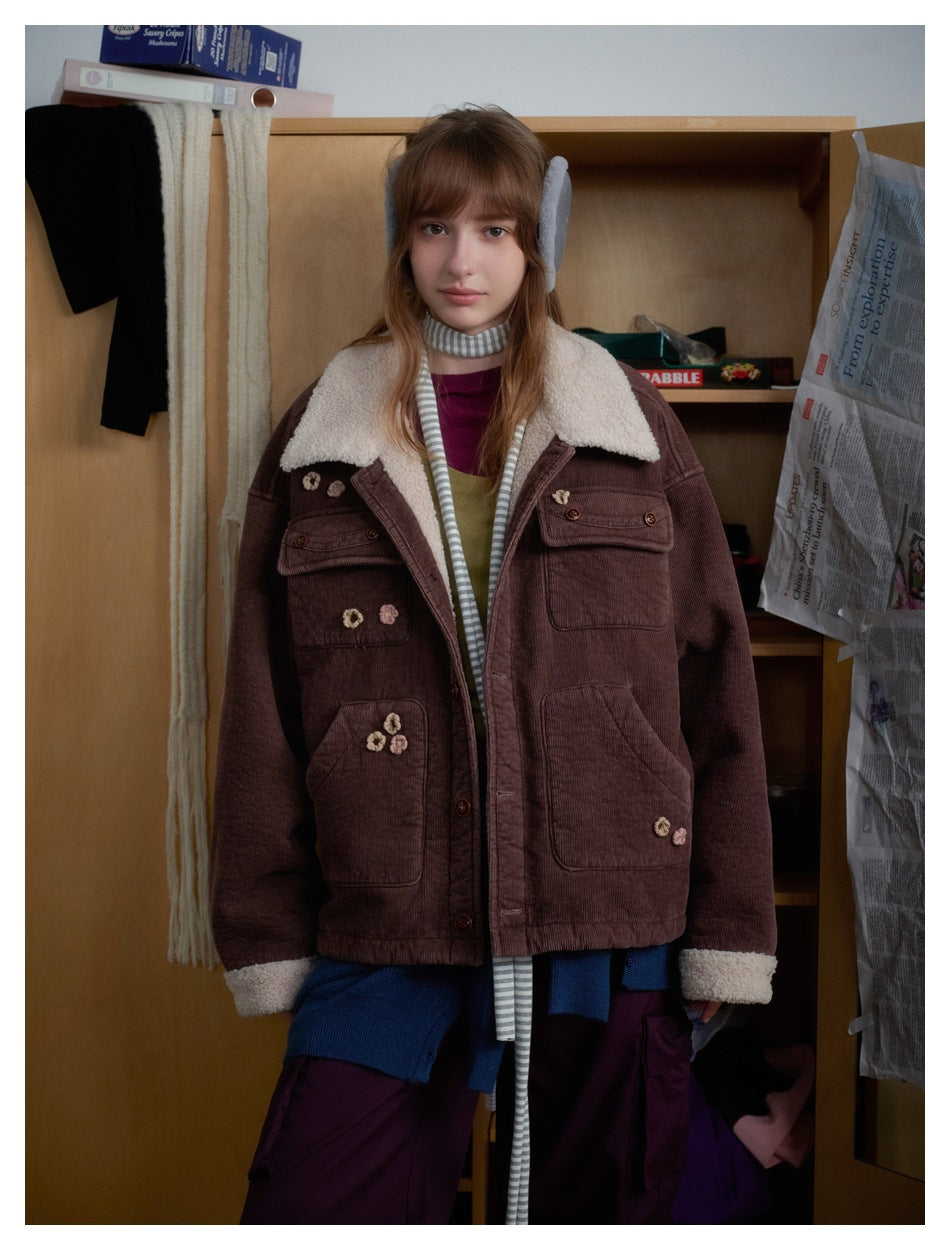 Model wearing a brown corduroy jacket with a cream shearling collar and cuffs, flower appliqués, and multiple pockets.