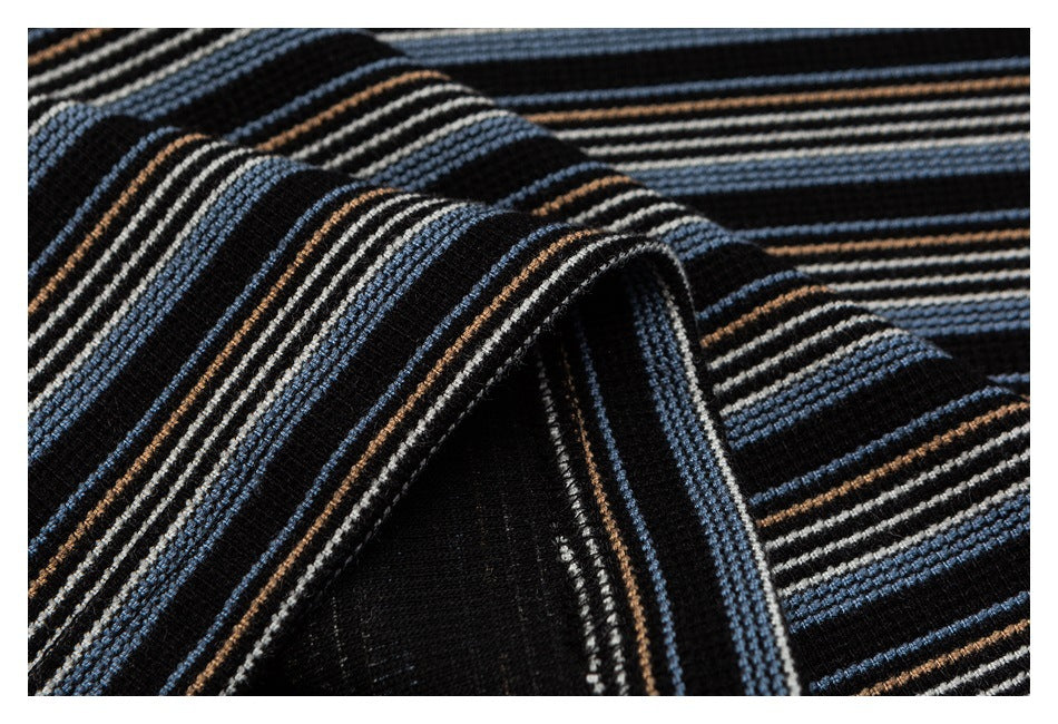 Close-up of black fabric with raised blue, cream, and brown stripes, folded to show the texture.