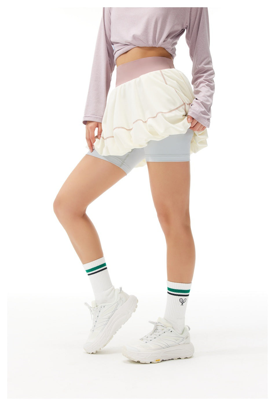 Model wearing a cream bubble tennis skirt with dusty pink waistband and pale gray built-in shorts, shown from the front.
