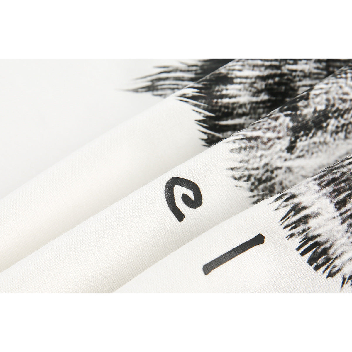 Close-up of white fabric with black abstract marks and a dense black-and-white feather-like print.