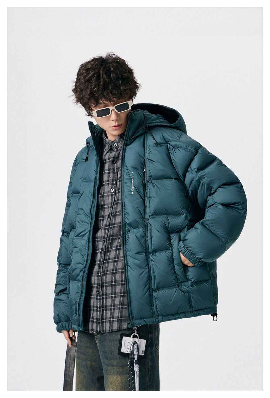 Model wearing an open teal hooded puffer jacket over a dark plaid shirt.