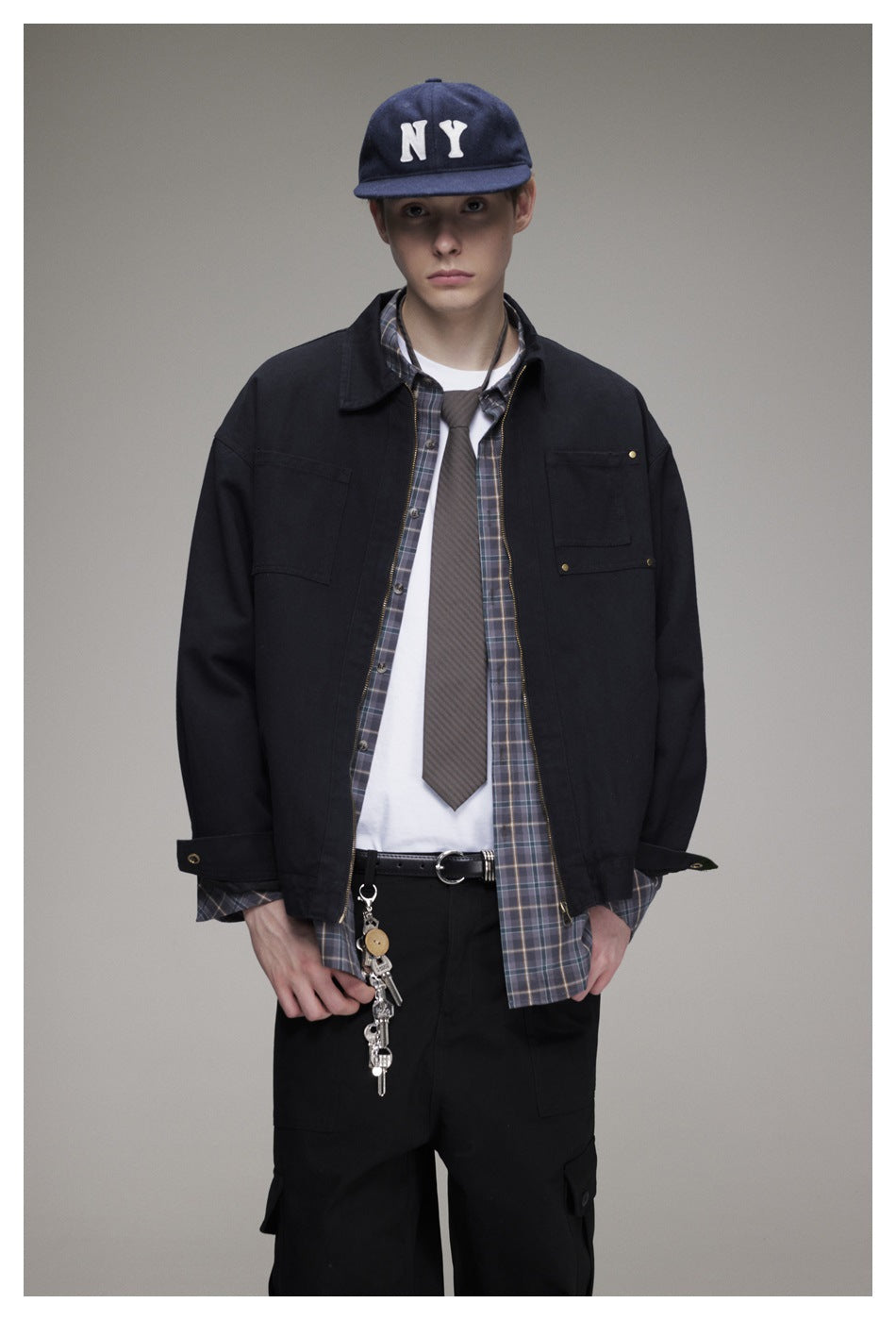 Front view of a model wearing a black zip-front jacket with chest pockets over a plaid shirt and white tee.