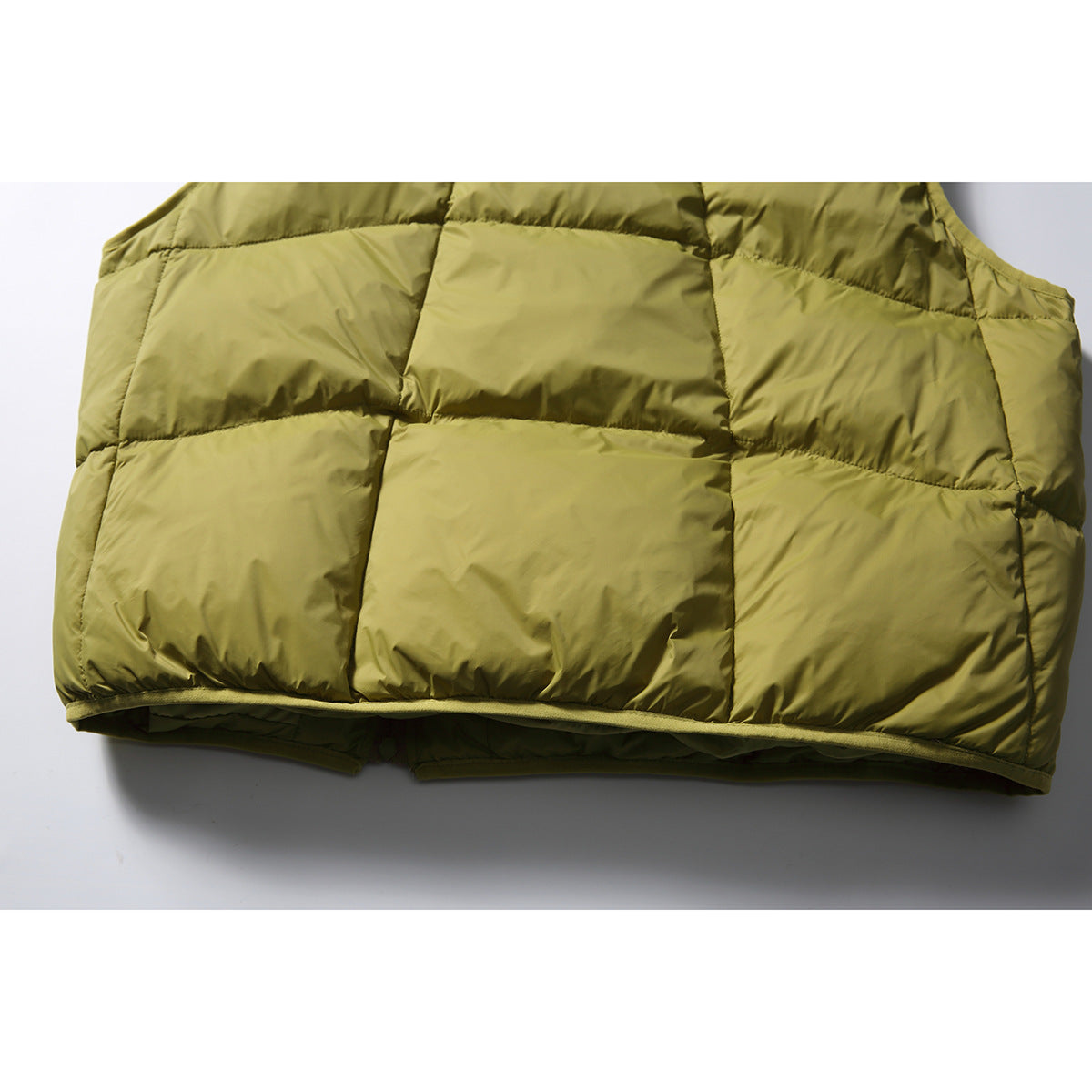Close-up of the olive-green puffer vest back, showing broad quilted panels and bound hem.