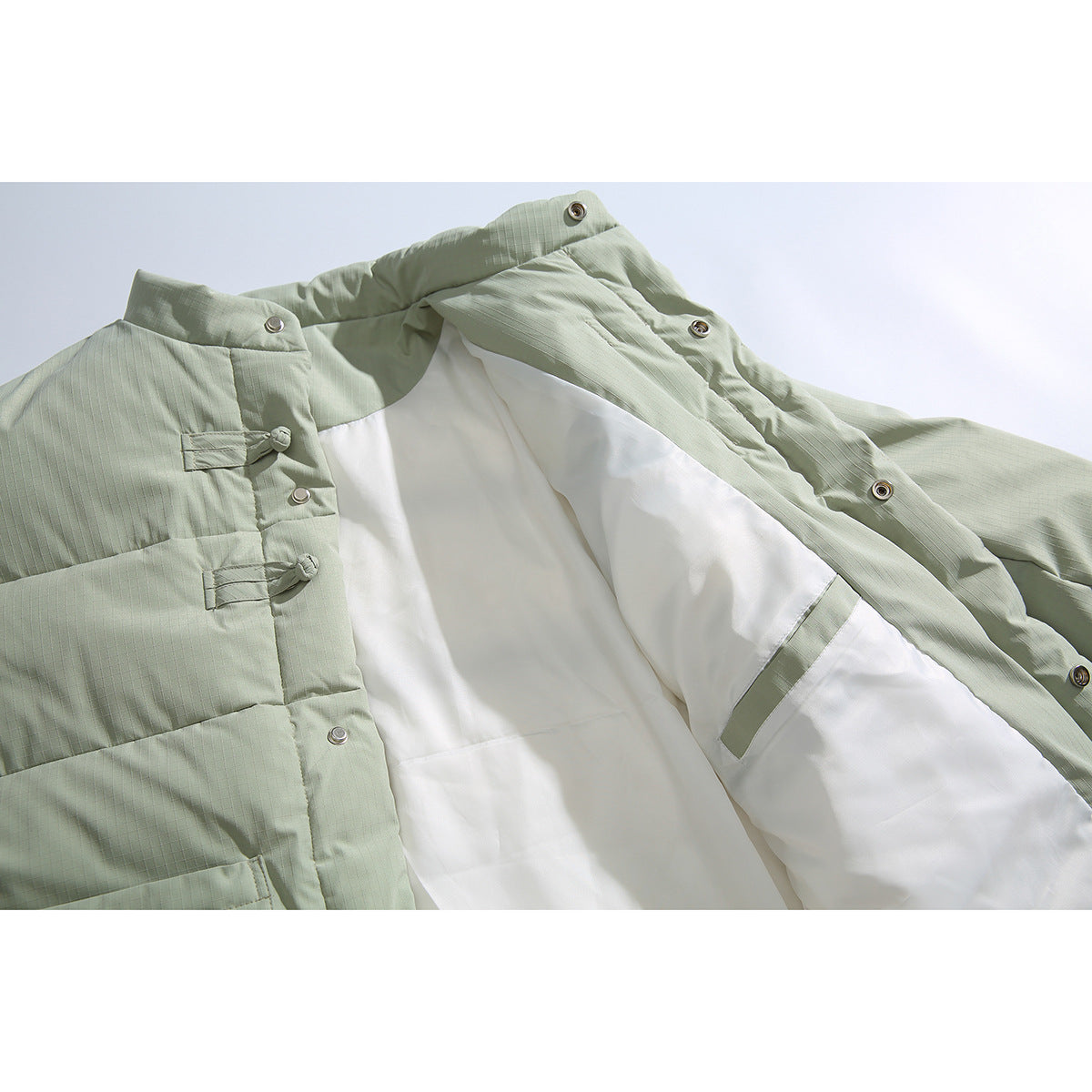 Open pale sage padded jacket showing its white lining, snap fasteners and fabric knot closures.