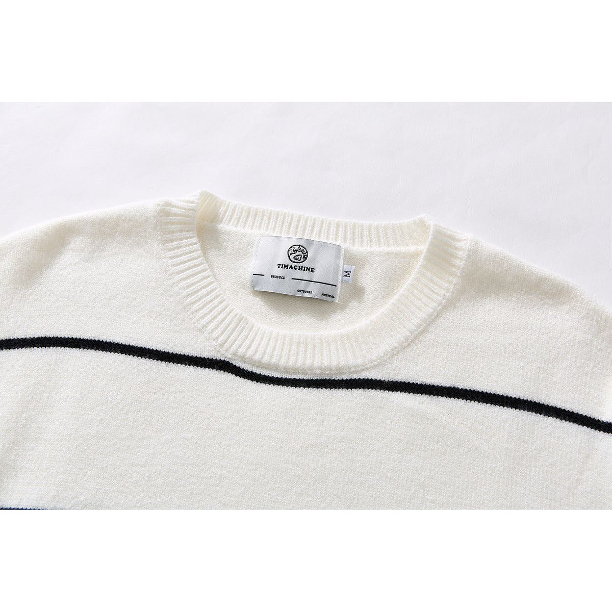 Close-up of an ivory knit sweater's ribbed crew neck and black horizontal stripe, with the sewn-in neck label visible.