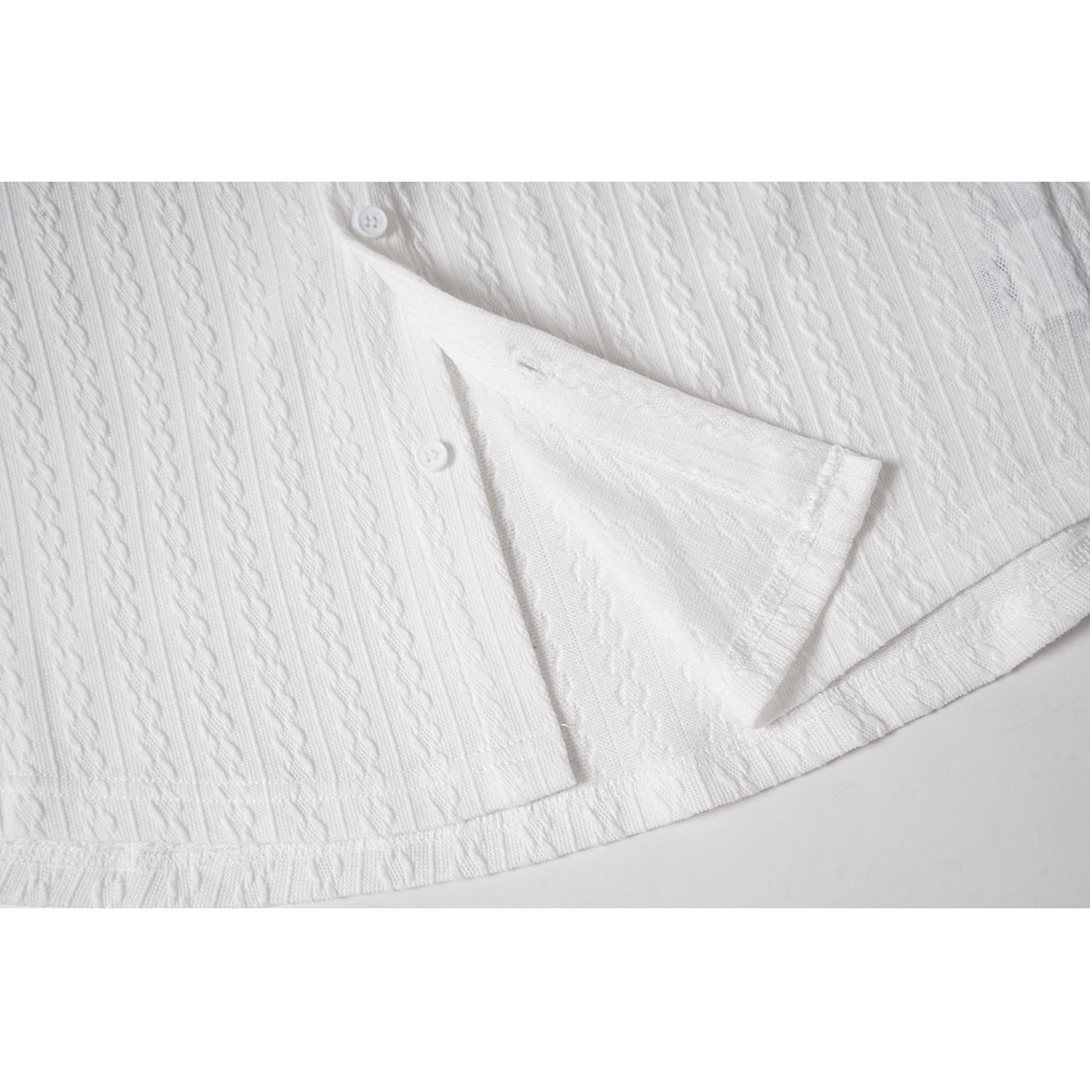 Close-up of a white shirt's textured knit hem and side slit with buttons visible above.
