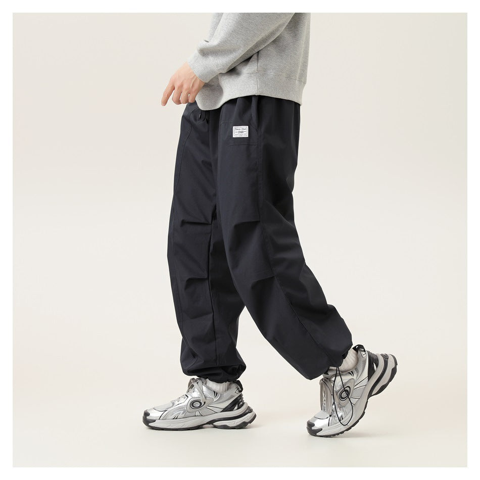 Model wearing loose black cargo-style pants in a side view, with a gray sweatshirt and sneakers.