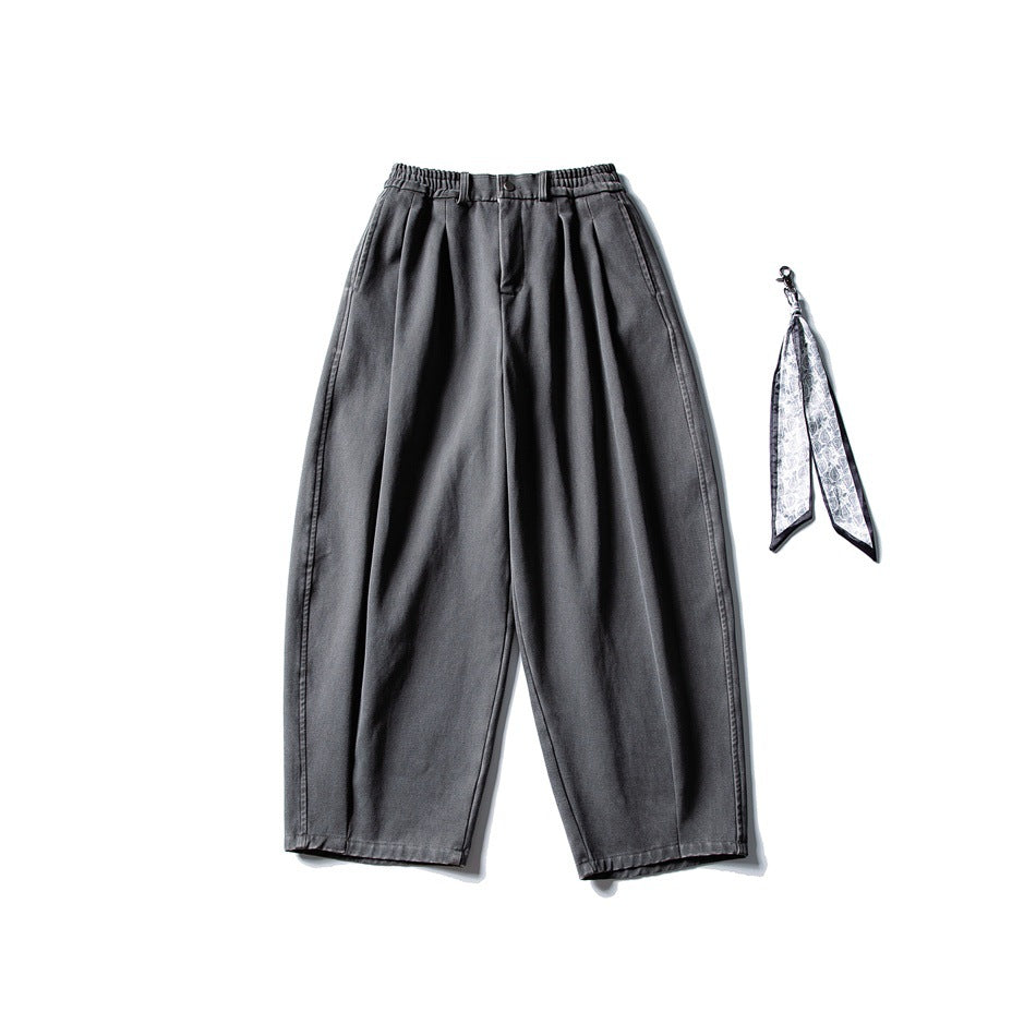 Gray wide-leg pleated pants with elastic waistband, flat lay, patterned scarf accessory beside them