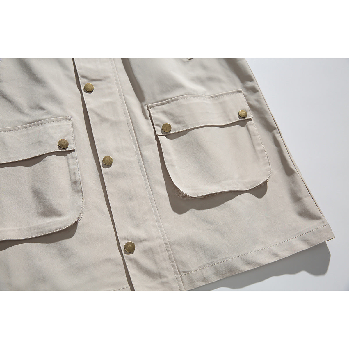 Close-up of the beige jacket's flap pockets, brass-tone snaps, front placket, and hem.