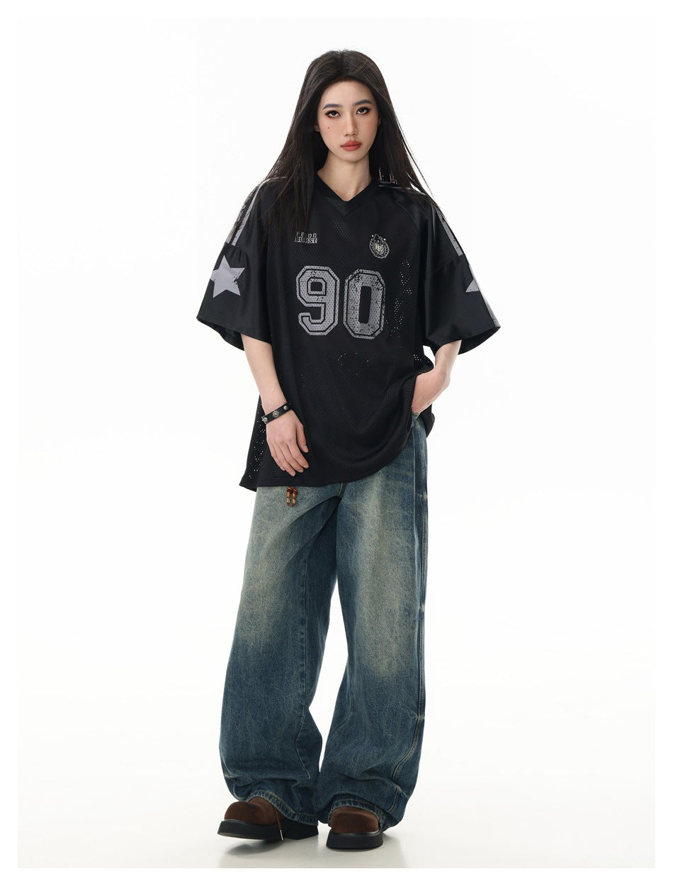 Model wearing an oversized black mesh V-neck jersey with gray number 90, star sleeve graphics, and loose blue jeans.
