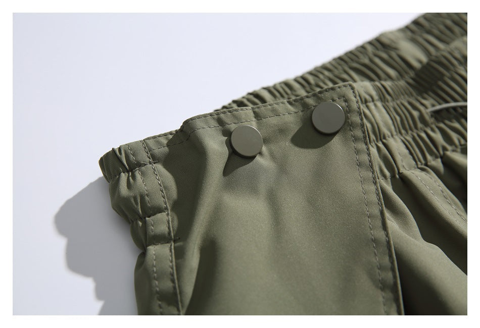 Close-up of two round snap buttons on an olive-gray pants waistband tab beside the gathered elastic waist.