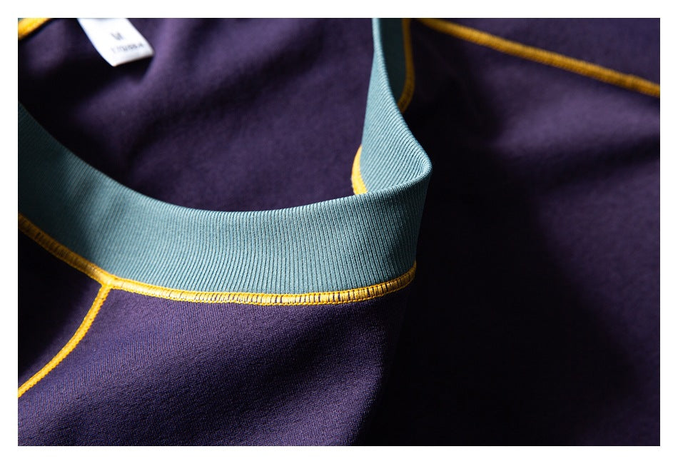 Close-up of a teal ribbed neckline on a purple garment with mustard-yellow stitching and a small white label.