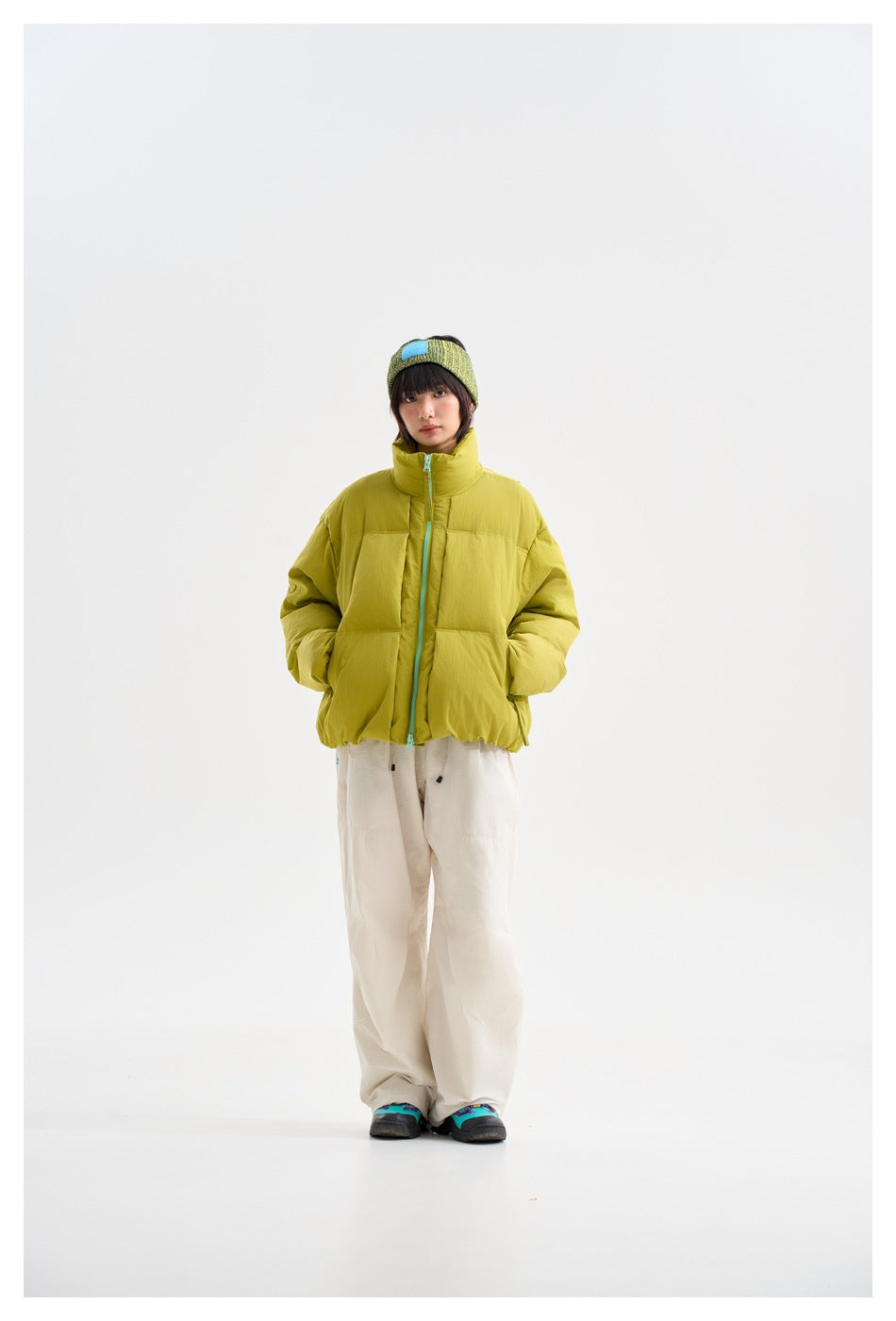 Model facing front in green puffer jacket with stand collar and light-blue zipper, with cream pants