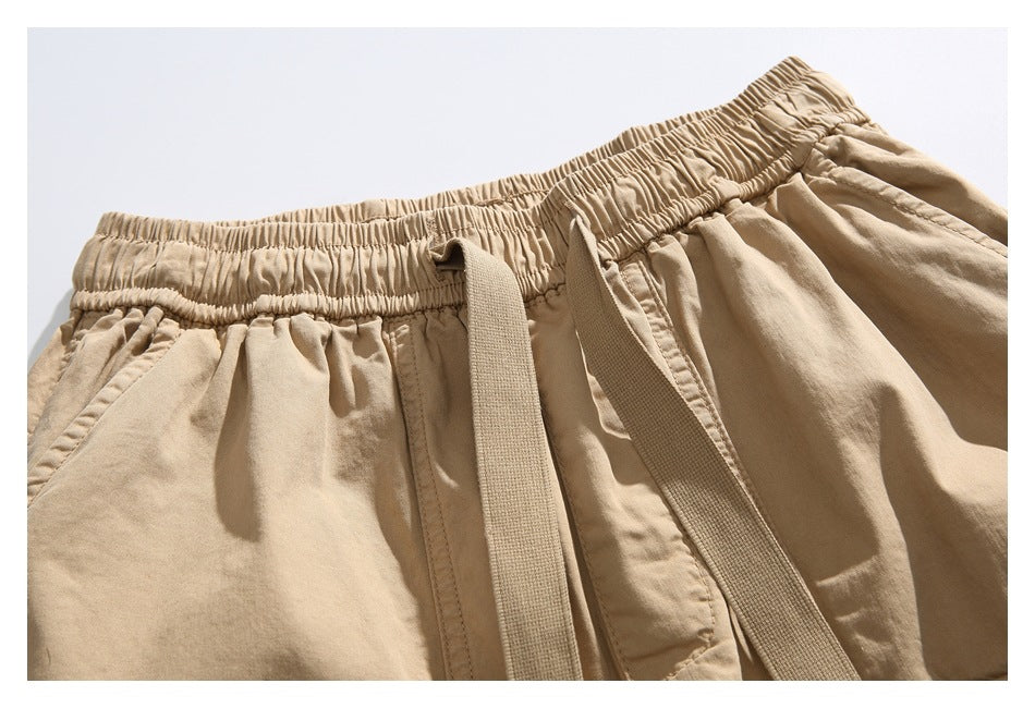 Close-up of tan shorts showing the gathered elastic waistband, drawstring and angled front pocket.
