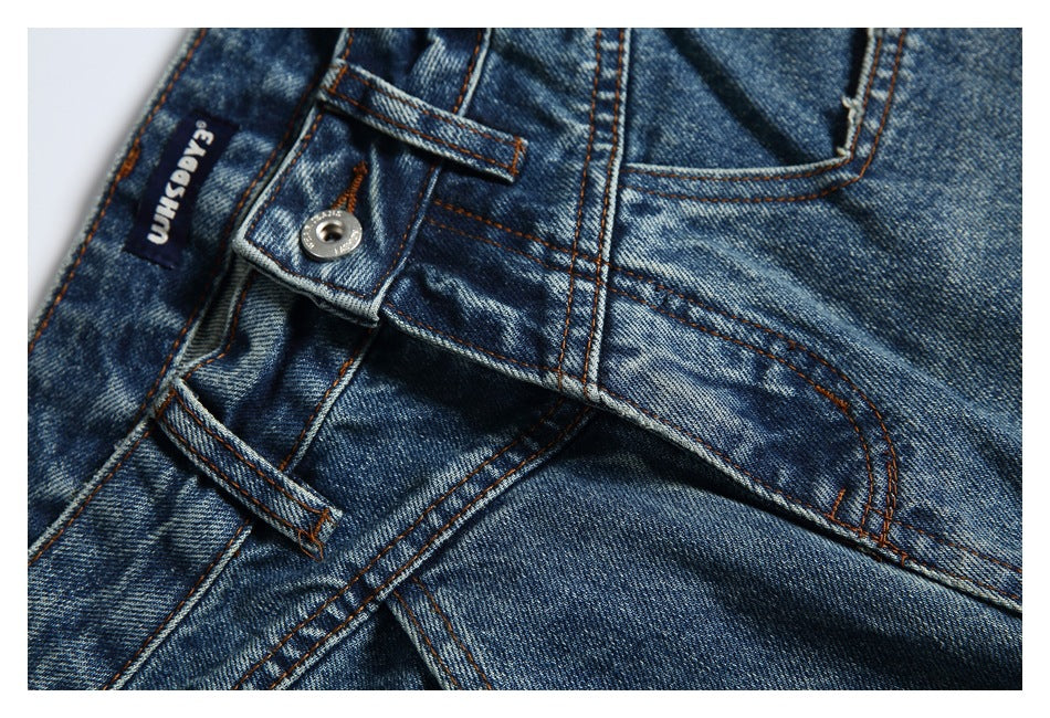 Close-up of faded blue jeans showing the waistband, button, belt loop, and orange-brown stitching.