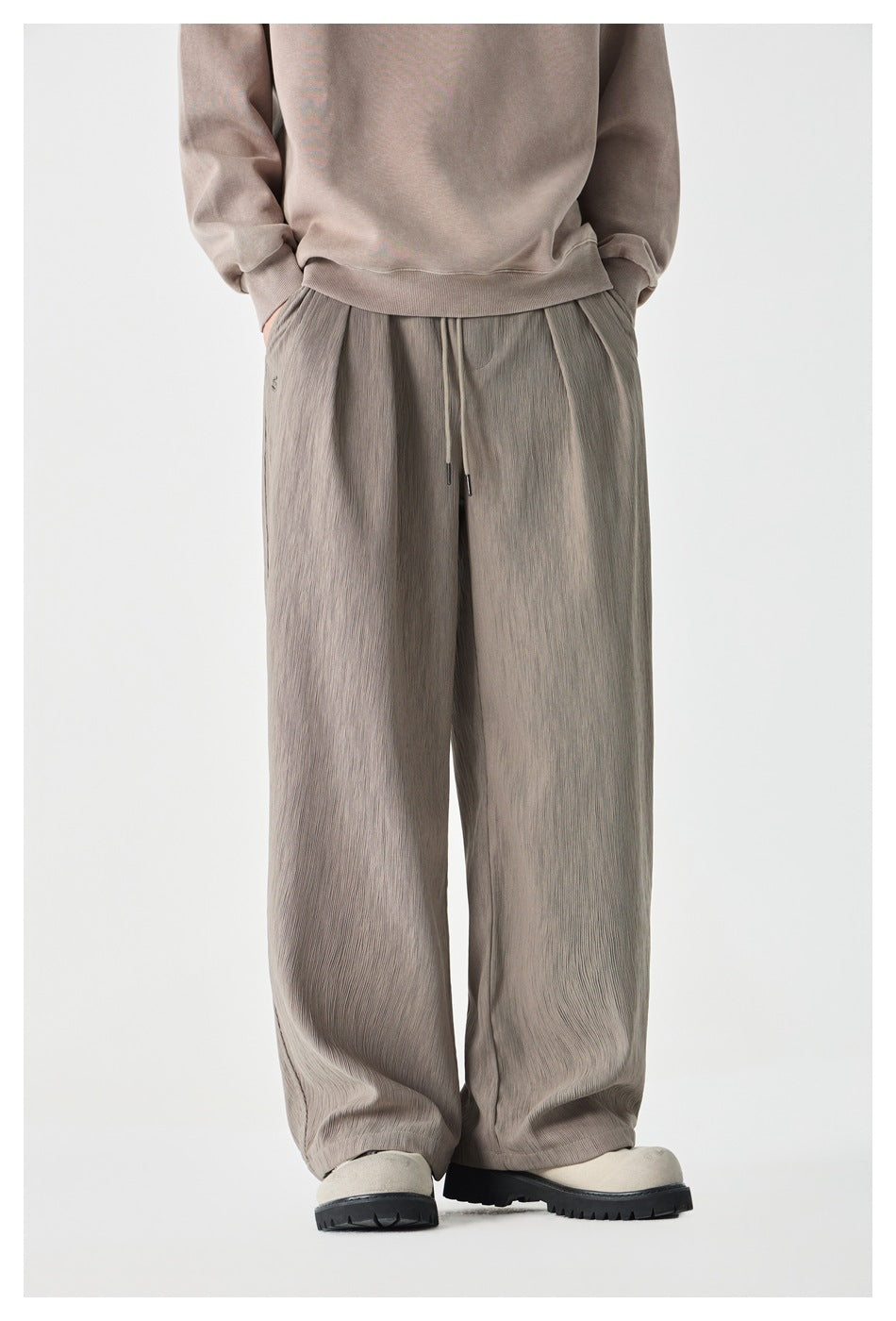 Front view of a model wearing taupe-gray wide-leg drawstring pants with a subtle crinkled texture.