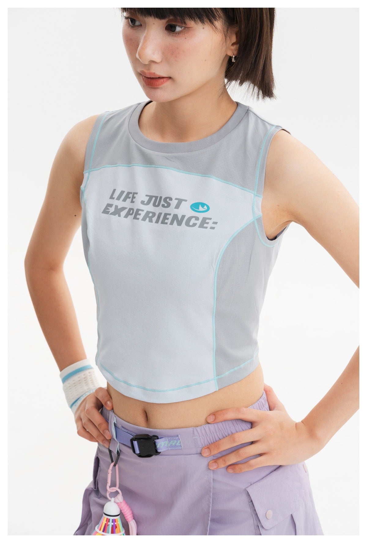 Close view of a model wearing a pale blue sleeveless crop top with aqua seam piping and a printed chest slogan.