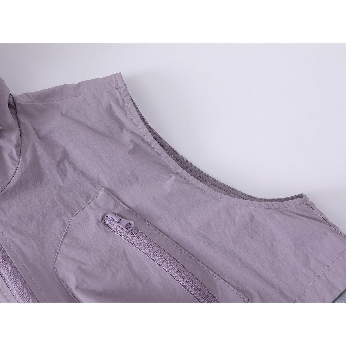 Close-up of the lavender vest's fabric and diagonal zip pocket.