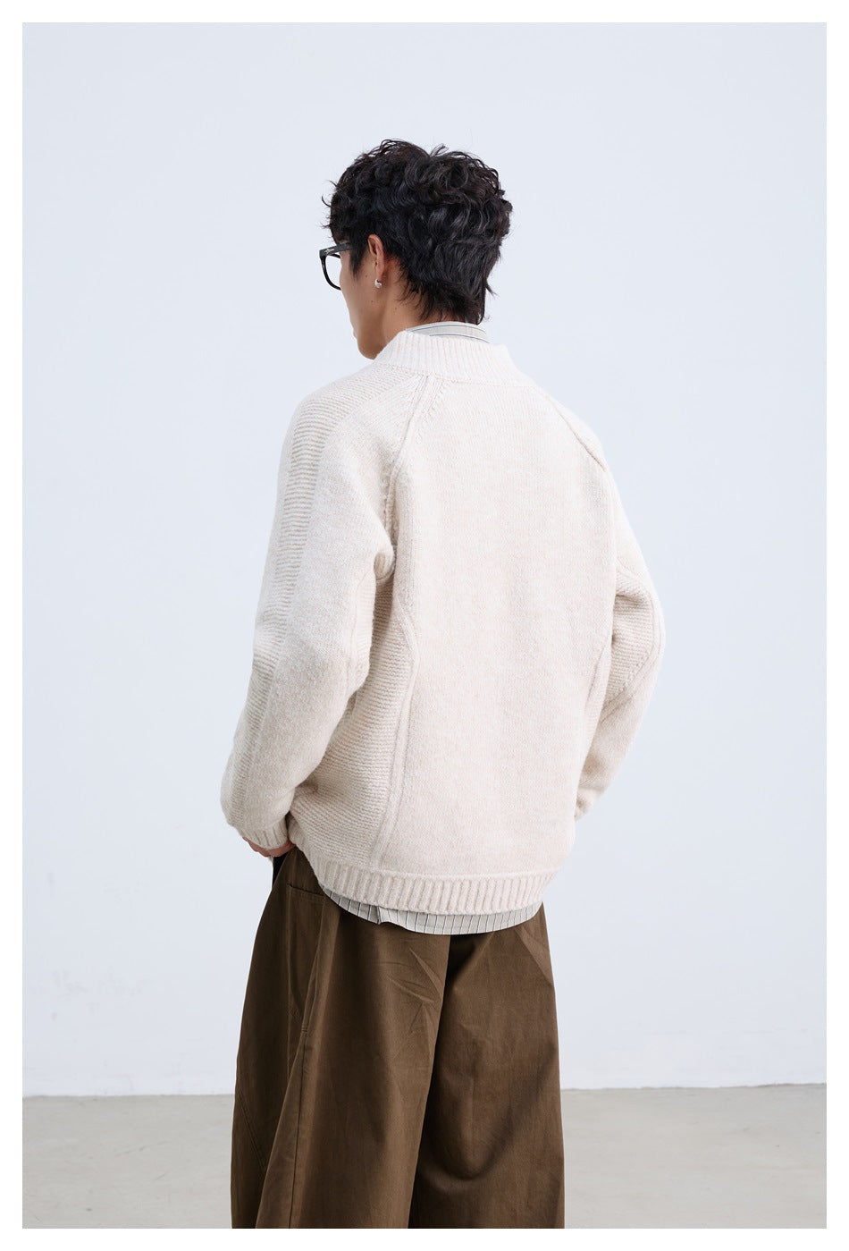 Rear view of a model wearing an off-white knit jacket with a stand collar and ribbed sleeve panels.