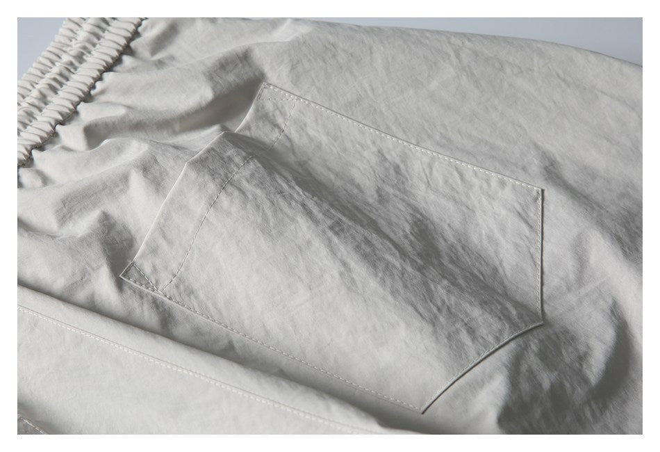 Close-up of a large stitched patch pocket on light gray shorts.