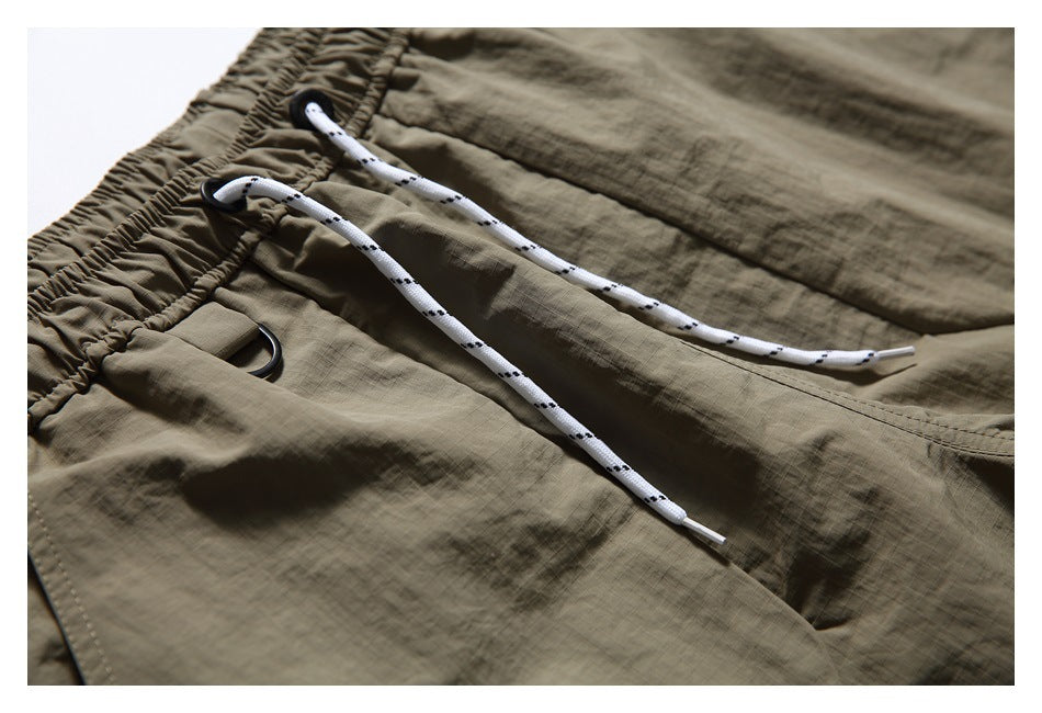 Close-up of olive-khaki shorts with a gathered waistband, white patterned drawstrings, and black metal loops.