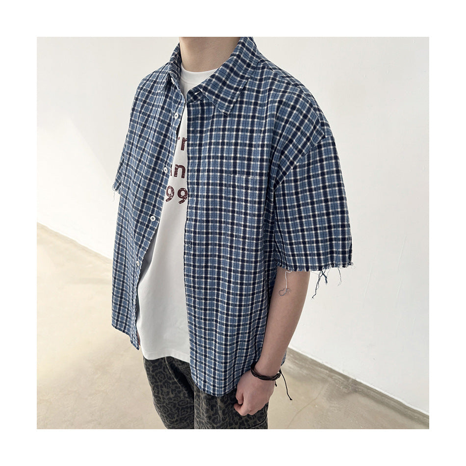 Close three-quarter view of the blue plaid short-sleeve shirt worn open over a white tee, showing the frayed sleeve hem