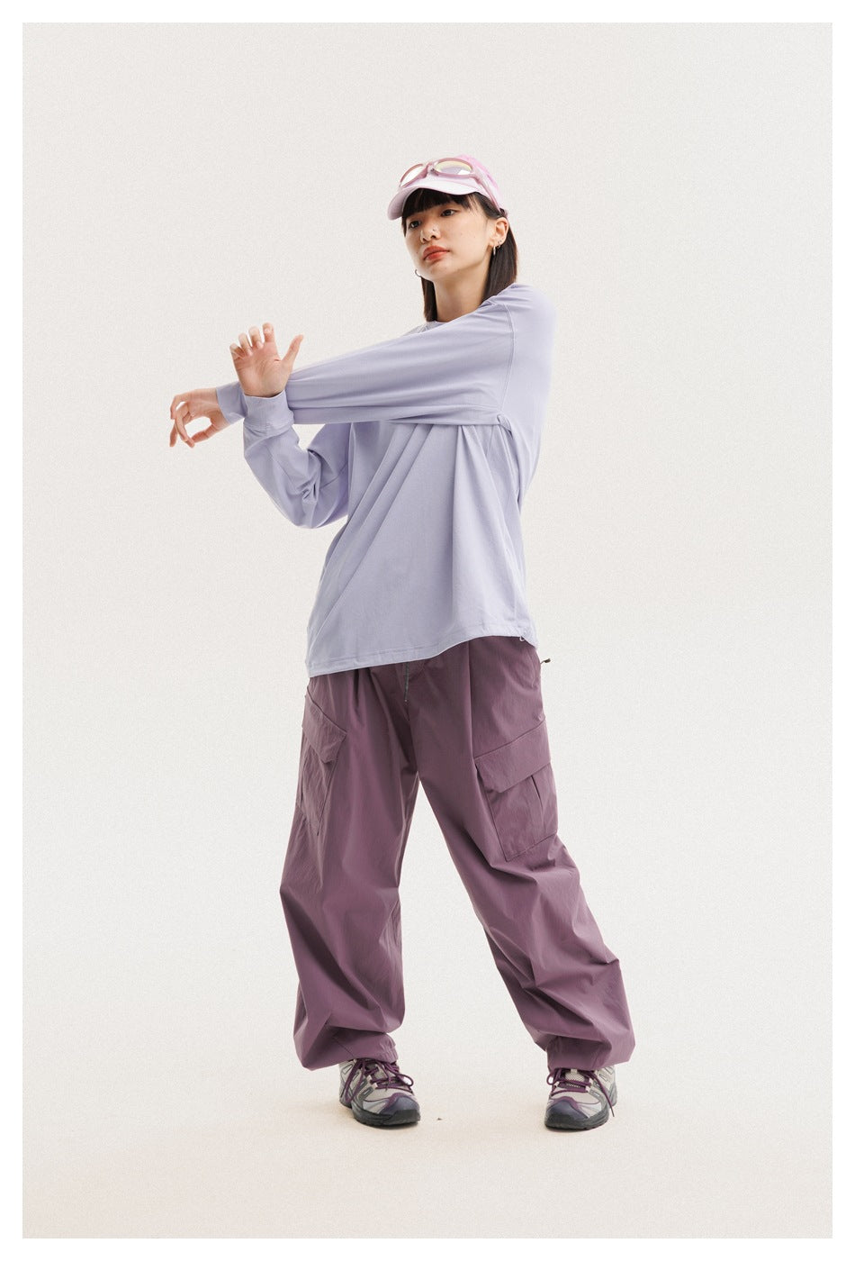 Model wearing a loose lavender long-sleeve shirt and mauve cargo pants, stretching one sleeve.