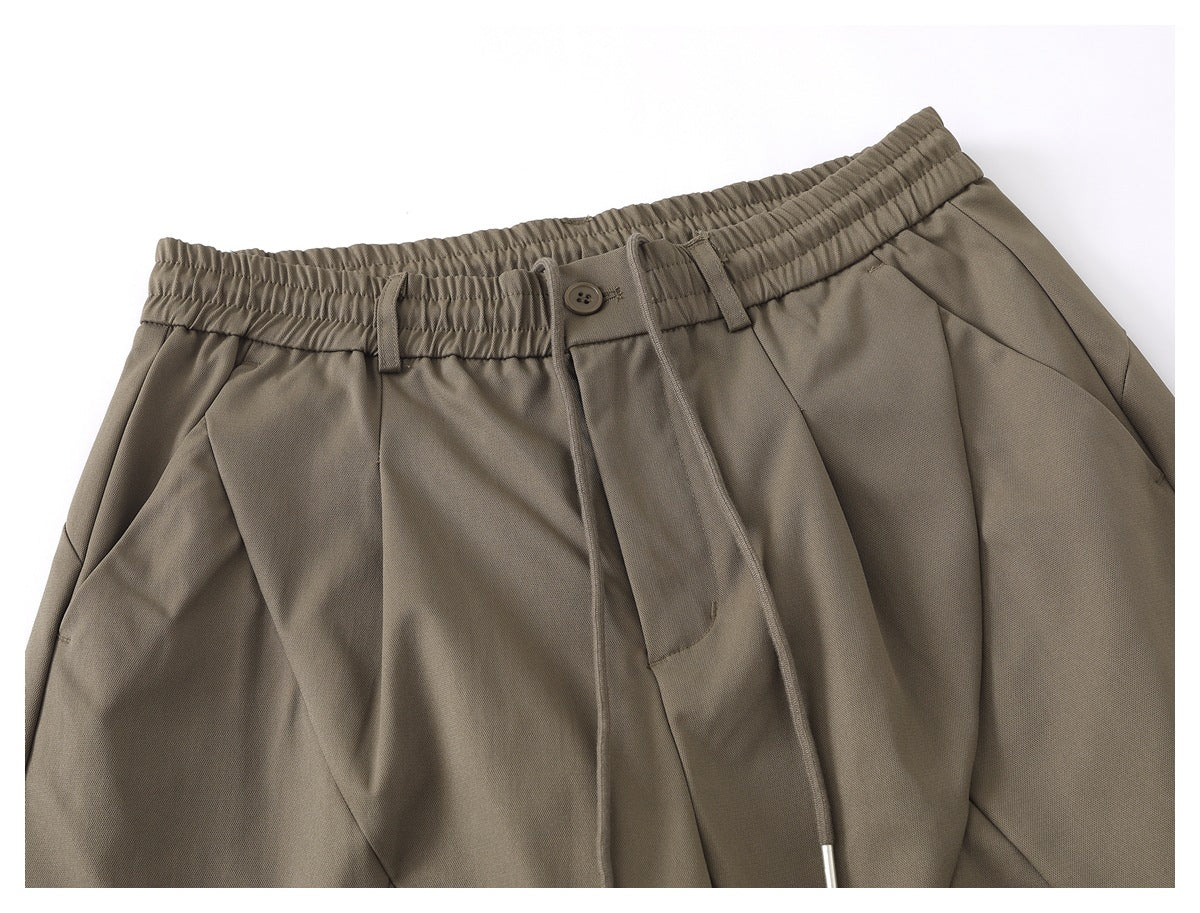 Cropped front view of taupe trousers with an elastic waistband, drawstring, belt loops, and front pockets.