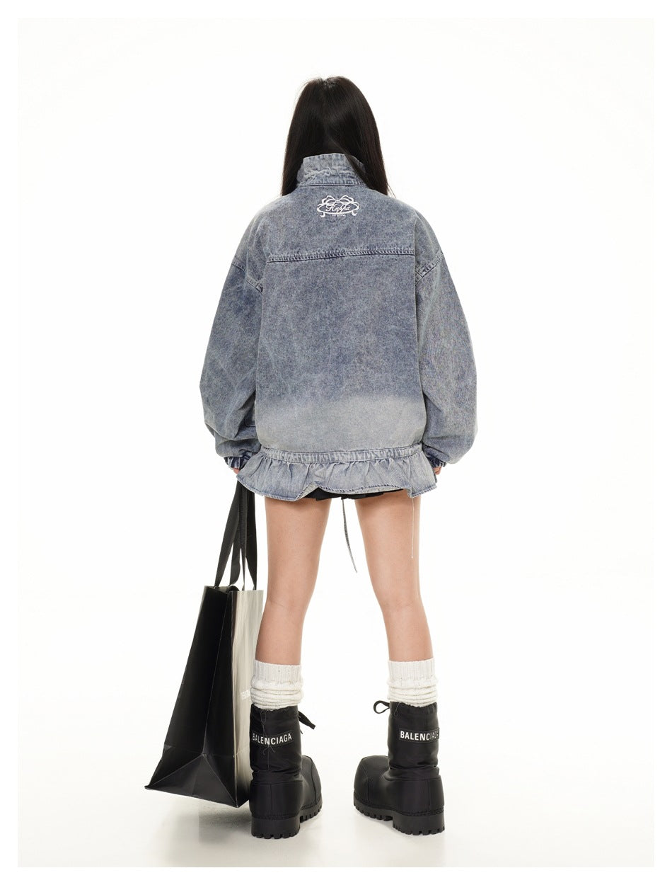 Rear view of a model wearing an oversized faded blue-gray denim jacket with a ruffled hem and small white back embroidery.