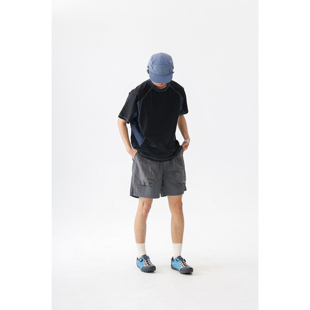 Model wearing a black short-sleeve shirt with blue-gray panels and dark gray cargo shorts against a white studio background.