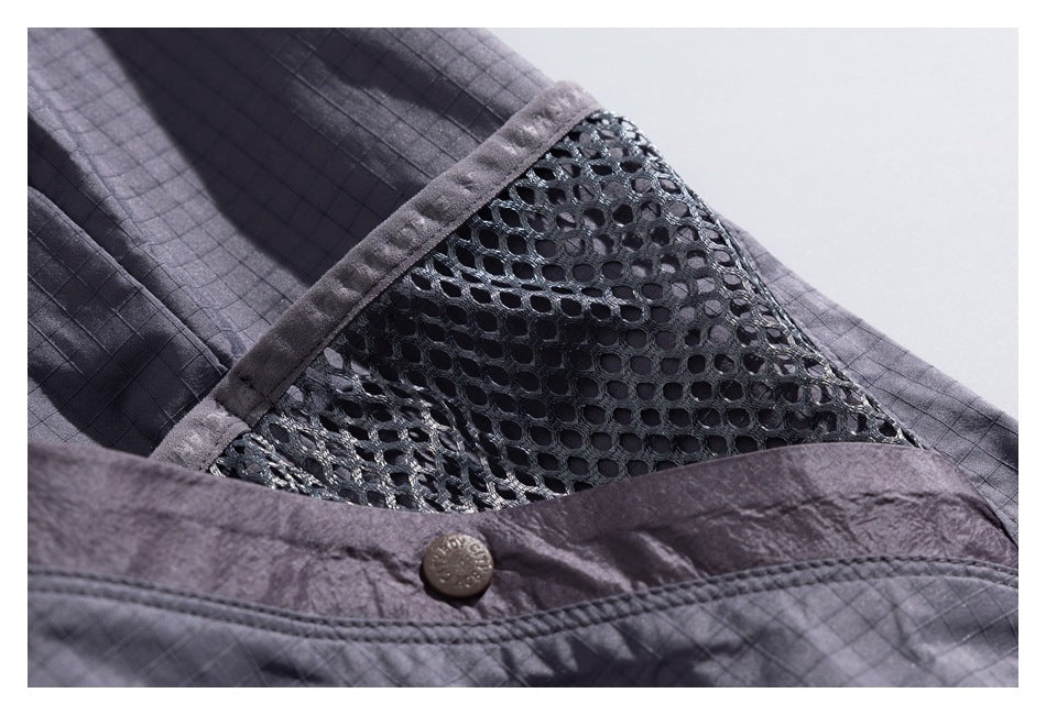 Close-up of a charcoal jacket's mesh panel, grid-patterned fabric, and snap-fastened edge.