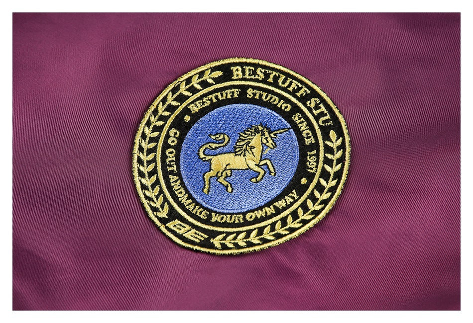 Close-up of a circular embroidered unicorn patch on plum jacket fabric.
