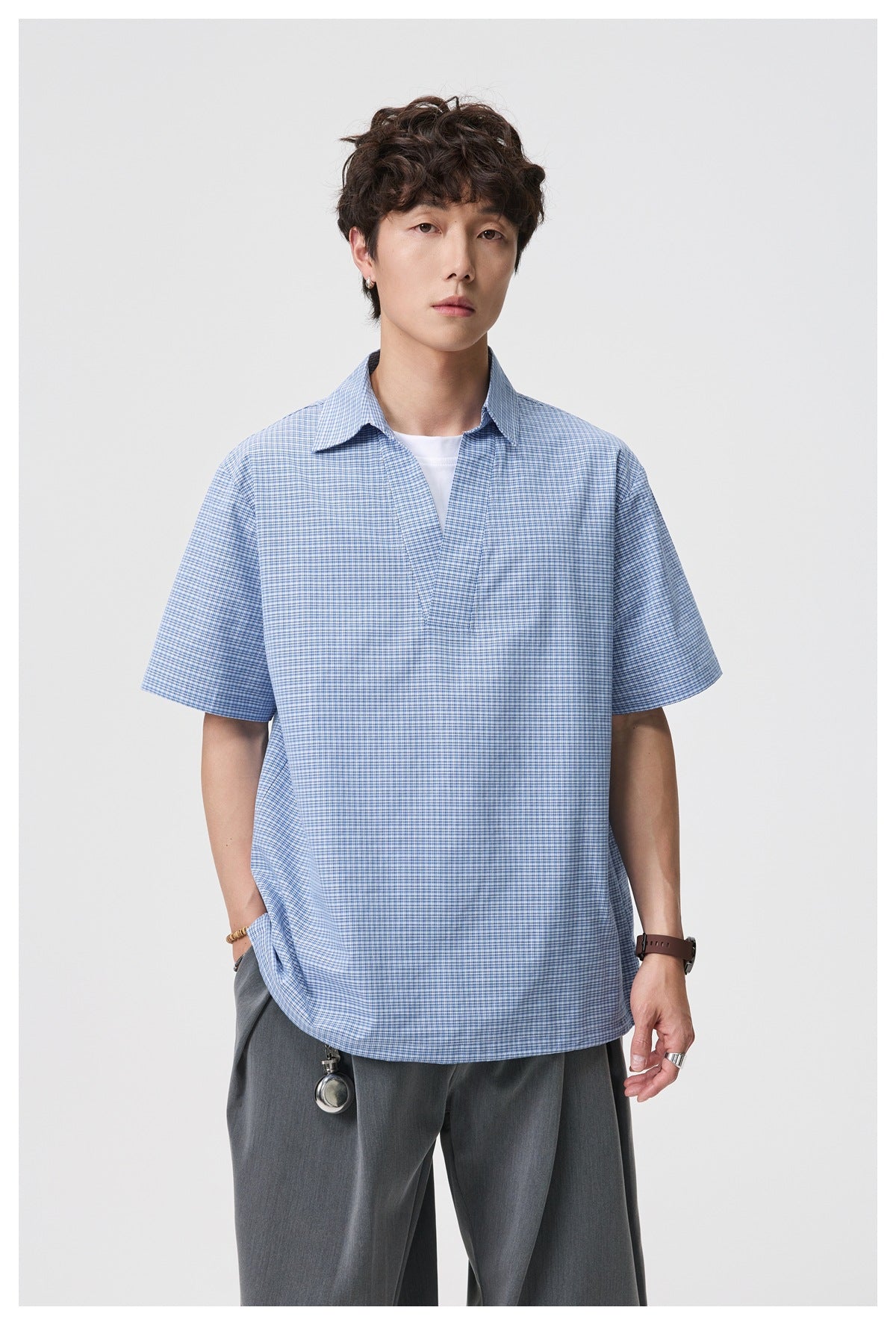 Model wearing blue check short-sleeve V-neck collared shirt with white layer and gray pleated trousers, front view