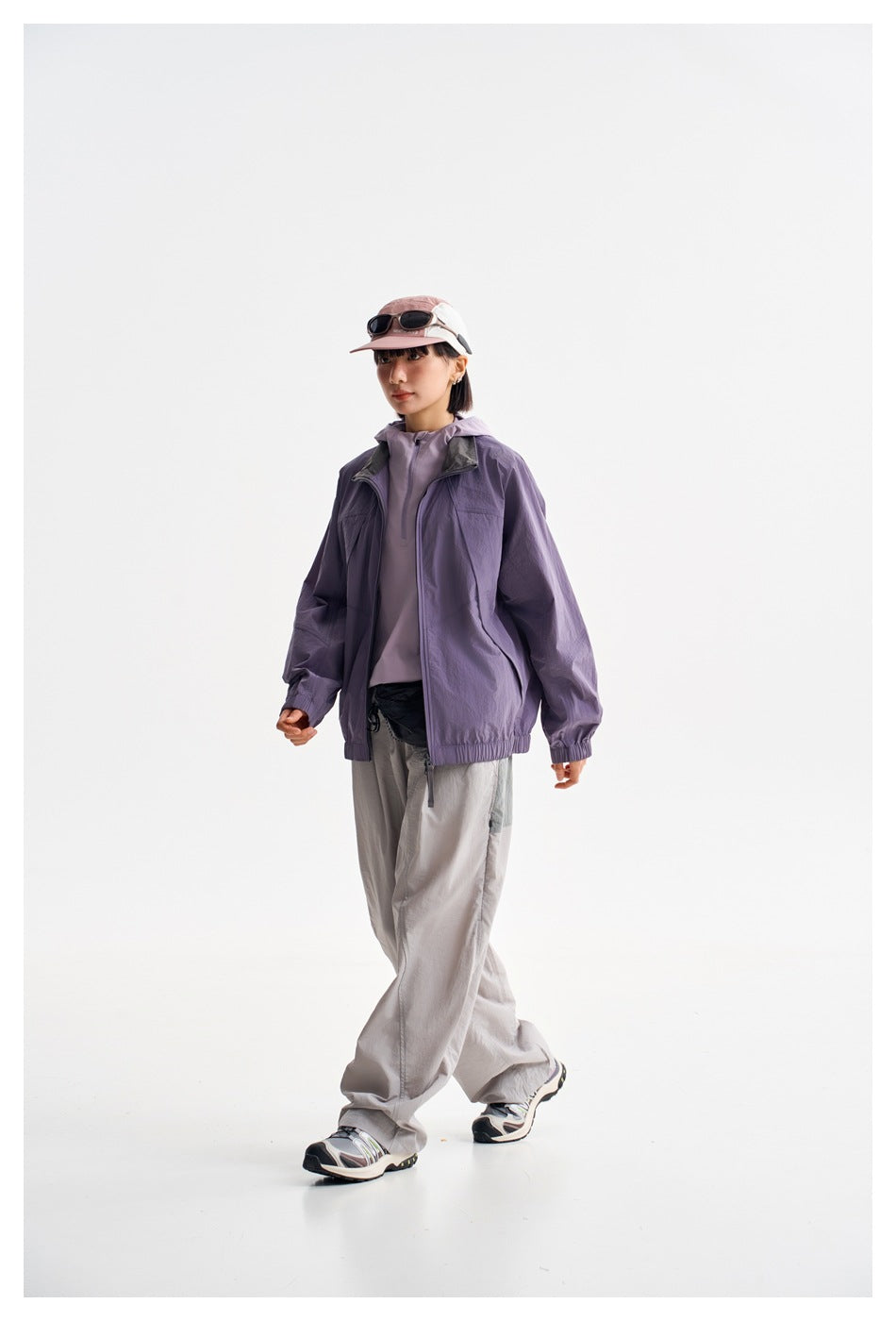 Model walking in a purple zip jacket with elastic cuffs and hem, shown from a three-quarter angle.