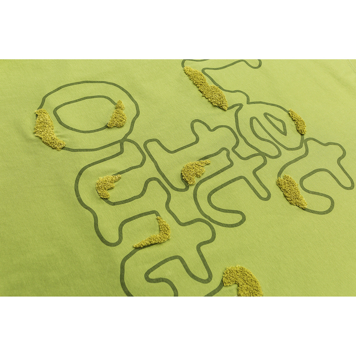 Close-up of a lime-green shirt with dark abstract line art and raised yellow embroidered accents.