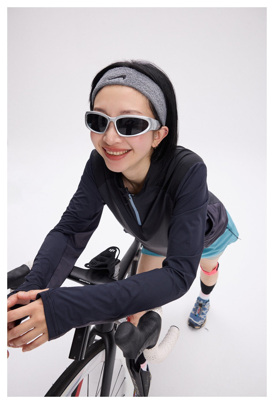 Woman leaning over a road bike in a dark color-block quarter-zip top and aqua shorts.