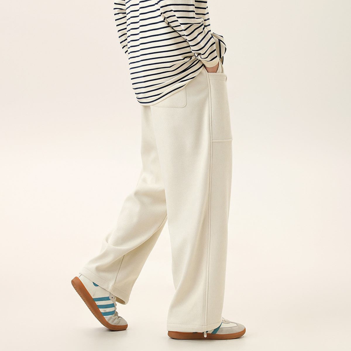 Model wearing wide-leg ivory ribbed pants with a side pocket and ankle zips, shown from the side.